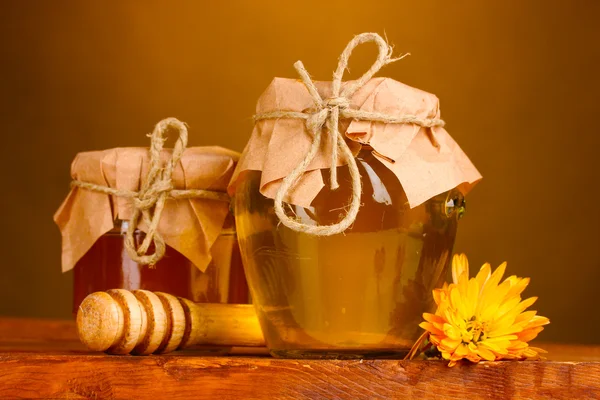 Two jars of honey and wooden drizzler on table on yellow background — Stock Photo, Image