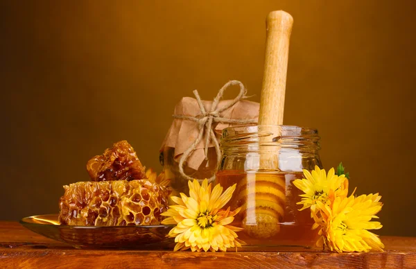 Two jars of honey,honeycombs and wooden drizzler on table on yellow backgro — Stock Photo, Image