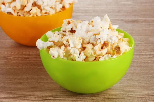 Popcorn in bright plastic bowls on wooden table — Stock Photo, Image