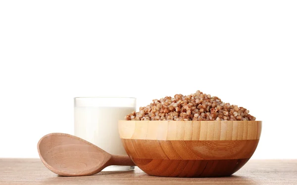 Boiled buckwheat in a wooden bowl with a glass of milk on wooden table isol — Stock Photo, Image