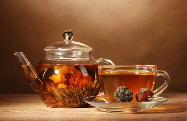 Стеклянный чайник и чашка с экзотическим зеленым чаем на деревянном столе на коричневом бэкгро — стоковое фото