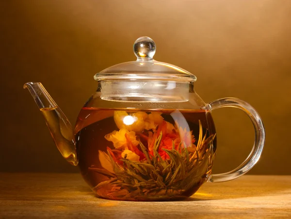 Théière en verre avec thé vert exotique sur table en bois sur fond brun — Photo