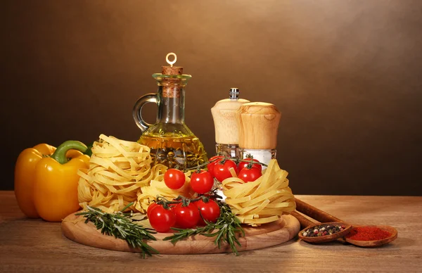 Makaron w misce, słoik, olej, przyprawy i warzywa na drewnianym stole na brązowy — Zdjęcie stockowe