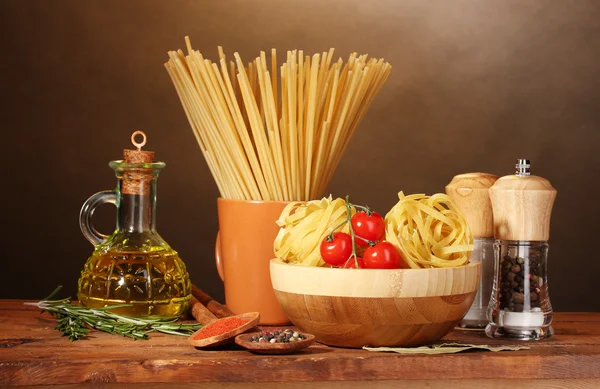 Spaghetti, Nudeln in Schüssel, ein Glas Öl und Gemüse auf einem Holztisch auf dem Tisch — Stockfoto