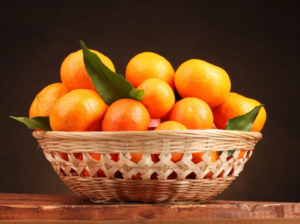 Mandarinas con hojas en una hermosa canasta sobre mesa de madera sobre respaldo marrón —  Fotos de Stock