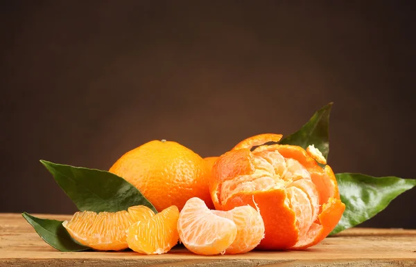 Tangerines with leaves on wooden table on brown background — Stock Photo, Image