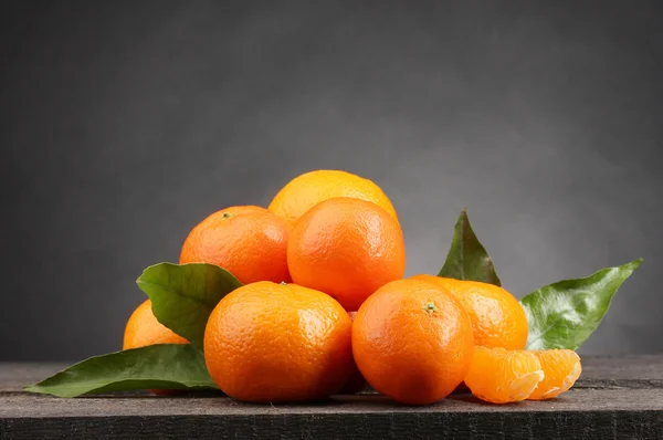 stock image Tangerines with leaves on wooden table on grey background