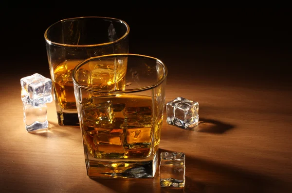 Dwie szklanki whisky szkockiej i lodu na drewnianym stole — Zdjęcie stockowe