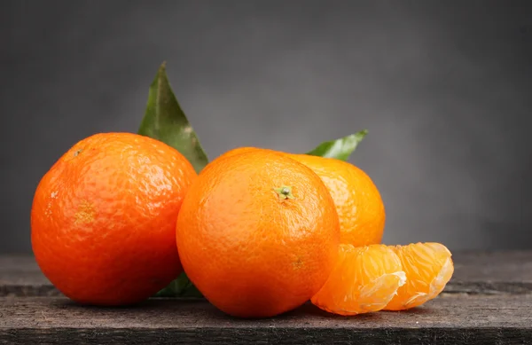 stock image Tangerines with leaves on wooden table on grey background