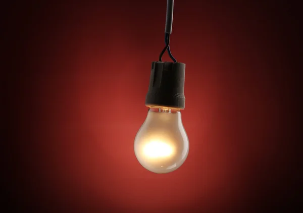 Una lampadina accesa su sfondo rosso — Foto Stock
