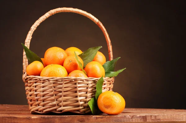 Tangerines with leaves in a beautiful basket on wooden table on brown backg Royalty Free Stock Images