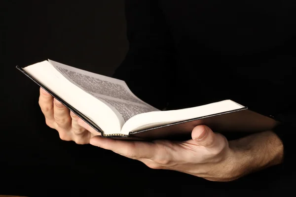 Manos sosteniendo la biblia rusa abierta sobre fondo negro — Foto de Stock