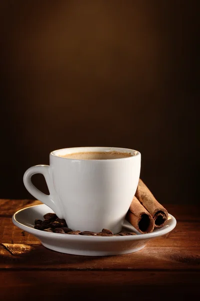 stock image Cup with coffee, cinnamon and coffee beans on wooden table on brown backgr