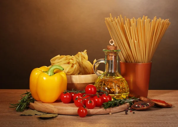 Spaghetti, noodles in bowl, jar of oil and vegetables on wooden table on br — Stock Photo, Image