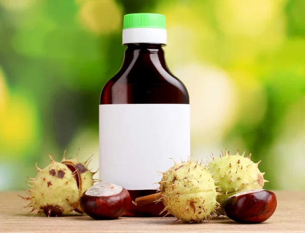 Chestnuts and medical bottle on wooden table on green background — Stock Photo, Image