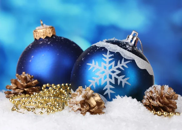Красиві блакитні різдвяні кульки і шишки в снігу на синьому фоні — стокове фото