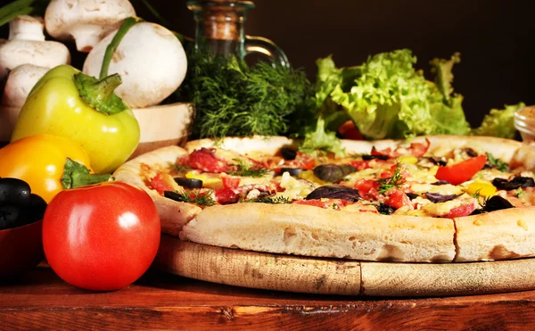 stock image Delicious pizza, vegetables and spices on wooden table on brown background