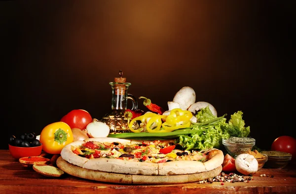 stock image Delicious pizza, vegetables and spices on wooden table on brown background