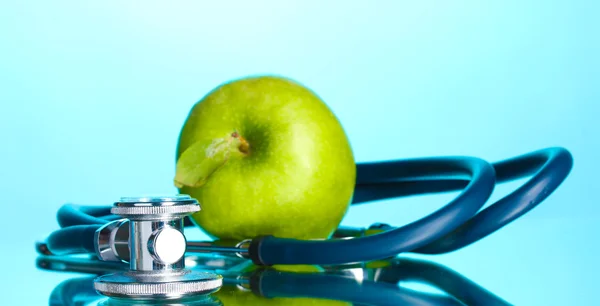 Medicinsk stetoskop och grönt äpple på blå — Stockfoto