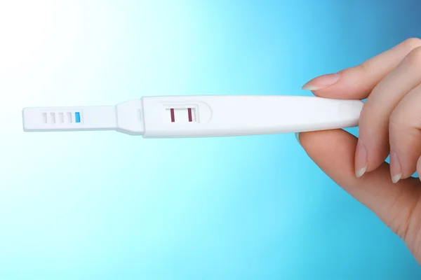 Teste de gravidez na mão sobre fundo azul — Fotografia de Stock