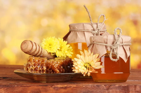 Due vasetti di miele, favi e drizzler in legno sul tavolo su fondo giallo — Foto Stock