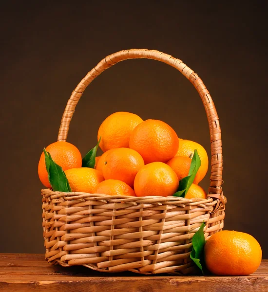Tangerines avec feuilles dans un beau panier sur table en bois sur fond marron — Photo