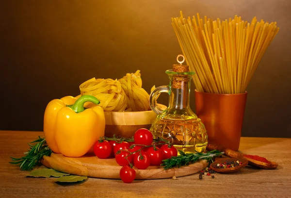 Spaghetti, tagliatelle in ciotola, vasetto di olio e verdure su tavolo di legno su br — Foto Stock