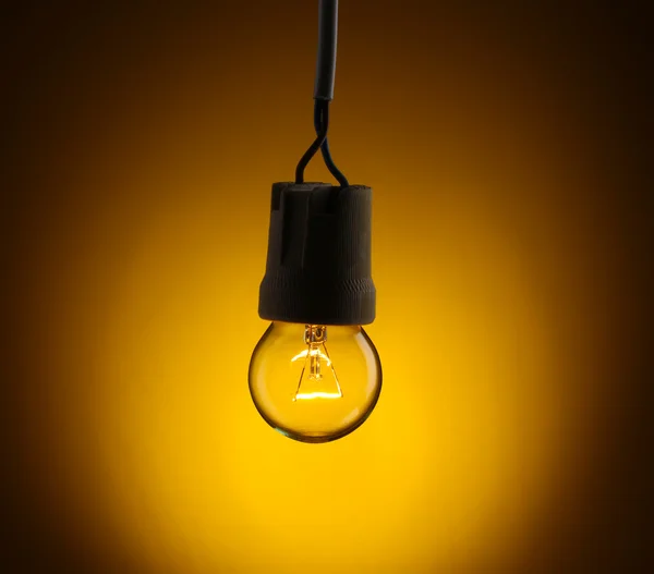 Uma lâmpada acesa no fundo amarelo — Fotografia de Stock