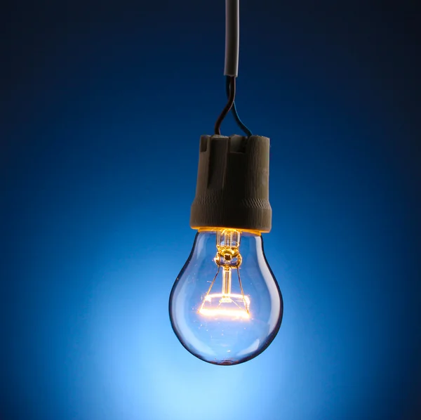 Una lampadina accesa su sfondo blu — Foto Stock