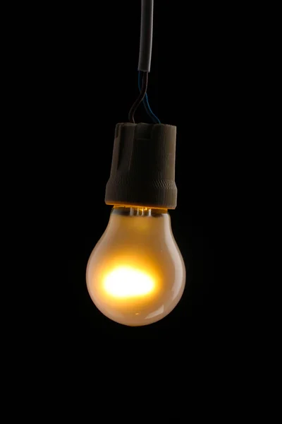 stock image A lit light bulb on black background