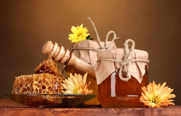 Dois jarros de mel, favos de mel e drizzler de madeira na mesa no backgro amarelo — Fotografia de Stock