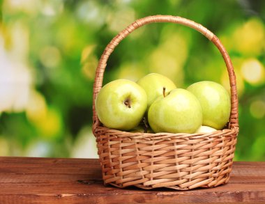 Juicy green apples in basket on wooden table on green background clipart