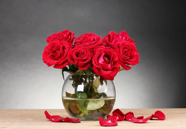 Hermosas rosas rojas en jarrón sobre mesa de madera sobre fondo gris —  Fotos de Stock