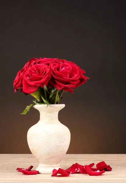 Belle rose rosse in vaso su tavolo di legno su sfondo marrone — Foto Stock
