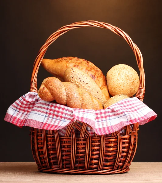 Delicious breads in basket on wooden table on brown background — Stock Photo, Image