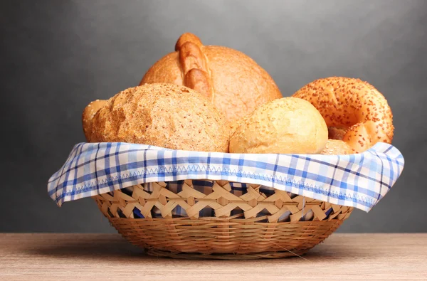 Delicious bread in basket on wooden table on gray background — Stock Photo, Image