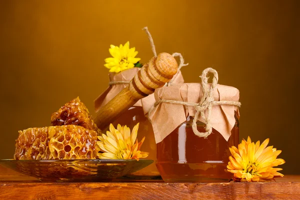 Dos tarros de miel, panales de miel y llovizna de madera en la mesa sobre fondo amarillo —  Fotos de Stock