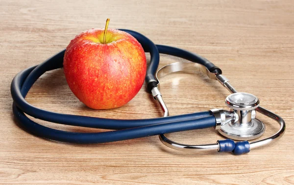 Медицинский стетоскоп и красное яблоко на деревянном фоне — стоковое фото