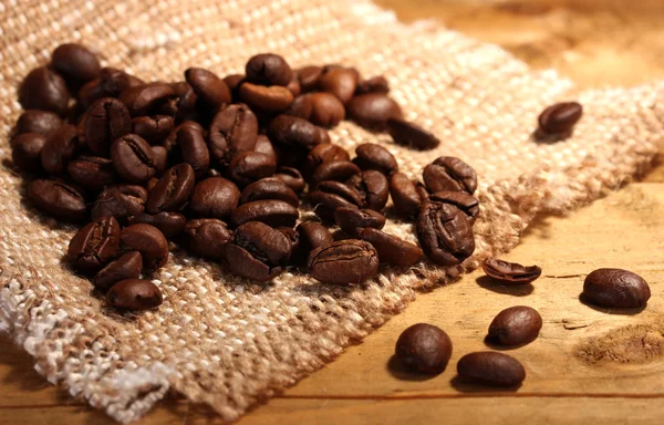 Grãos de café em saquear na mesa de madeira — Fotografia de Stock