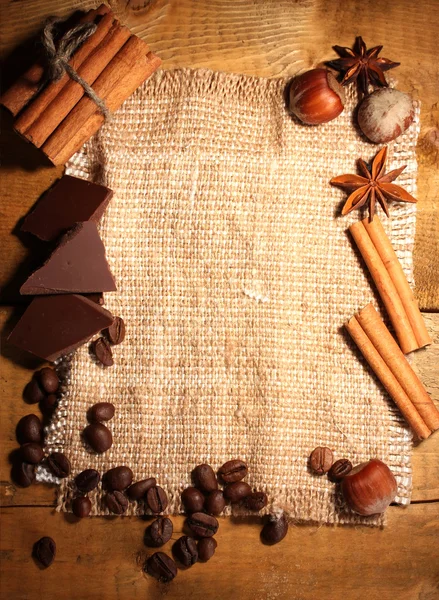 Кофейные зерна, коричные палочки, орехи и шоколад на мешочке на деревянной доске — стоковое фото