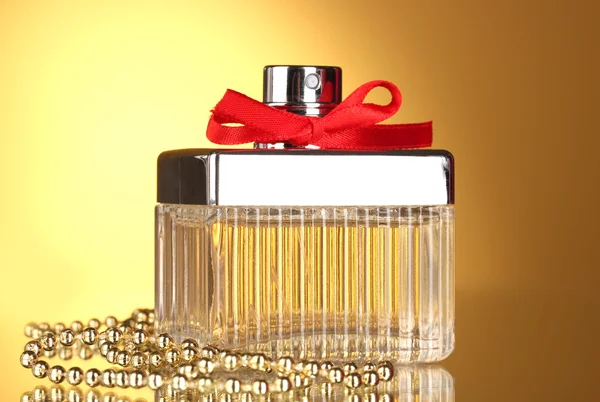 Perfume bottle with red bow on yellow background — Stock Photo, Image