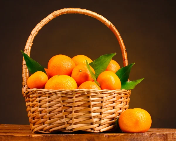 Tangerines with leaves in a beautiful basket on wooden table on brown backg Stock Photo