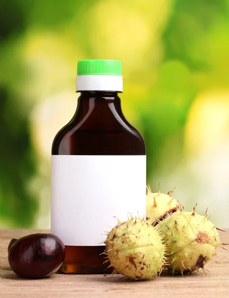 Каштаны и медицинская бутылка на деревянном столе на зеленом фоне — стоковое фото