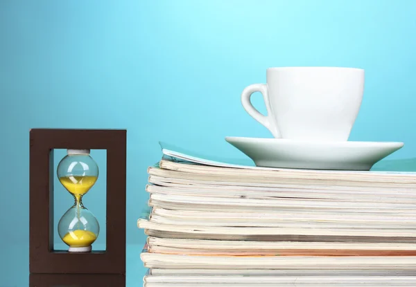 Stack av tidskrifter, cup och timglas på blå bakgrund — Stockfoto