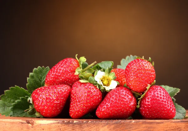 Strawberries with leaves on wooden table on brown background — Stock Photo, Image