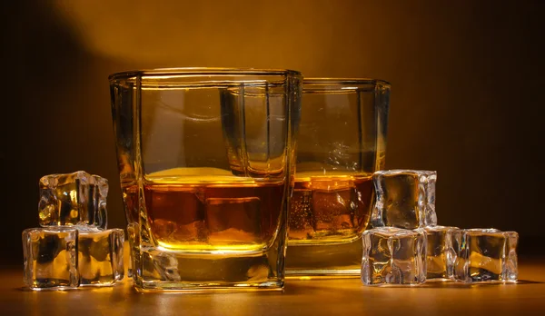 Dos vasos de whisky escocés y hielo sobre mesa de madera sobre fondo marrón — Foto de Stock