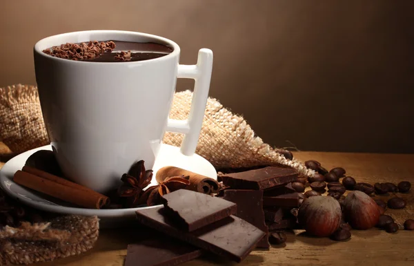 Xícara de chocolate quente, paus de canela, nozes e chocolate na mesa de madeira o — Fotografia de Stock