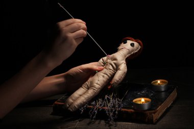 Voodoo doll girl pierced by a needle on a wooden table in the candlelight clipart