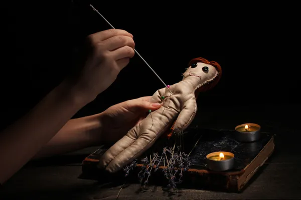 Voodoo docka flicka genomborrad av en nål på ett träbord i levande ljus — Stockfoto