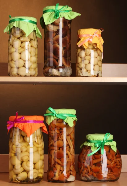 Deliciosos champiñones marinados en los frascos de vidrio en estantes de madera —  Fotos de Stock